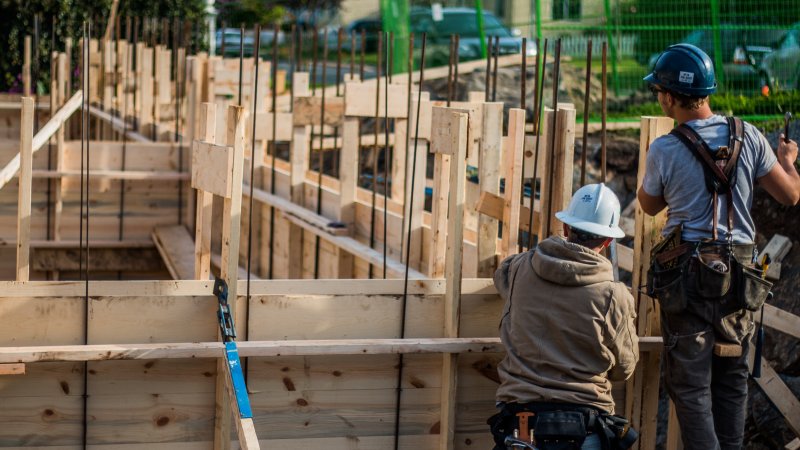 two construction workers beside a house frame