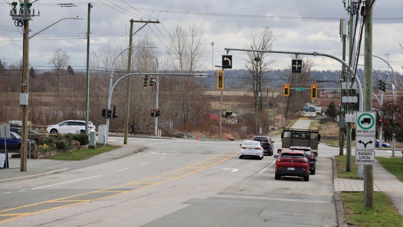 A street view with traffic lights, vehicles, and a pedestrian, under an overcast sky.