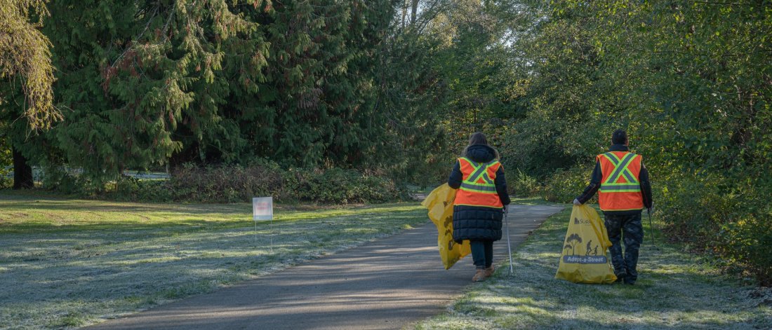 two volunteers in visi vests collect garbage in a park